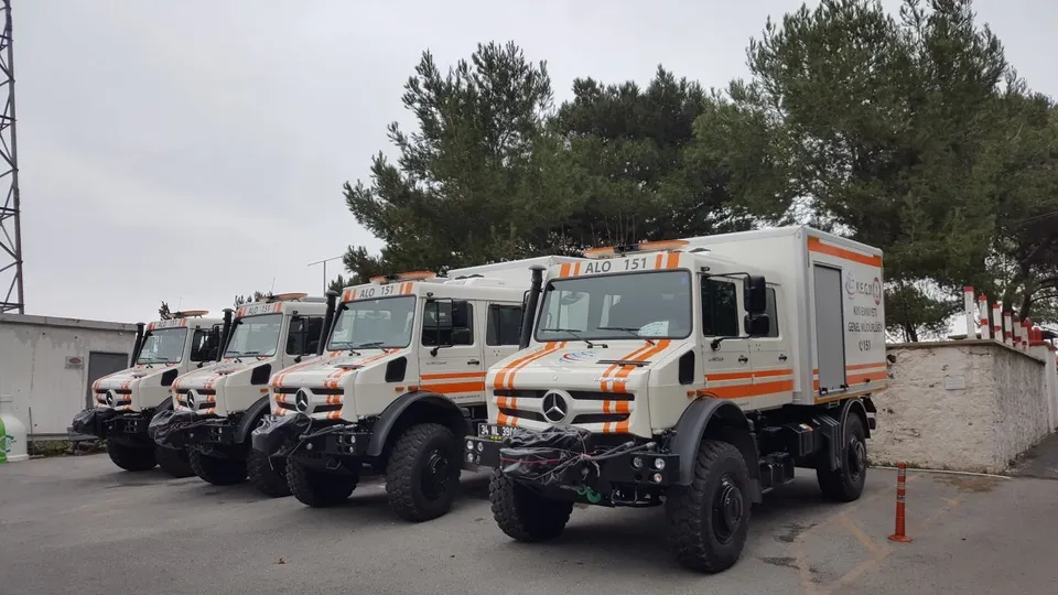 Turuncu şeritli arazi tipi hizmet kamyonlarından oluşan giydirilmiş filo, önden görünüm.
