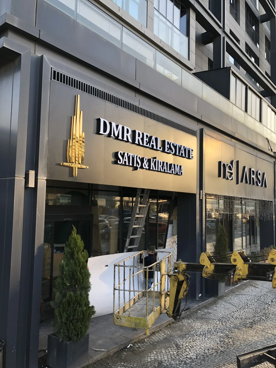İş merkezi girişinde altın renkli kurumsal cephe harfleri ve logolar.
