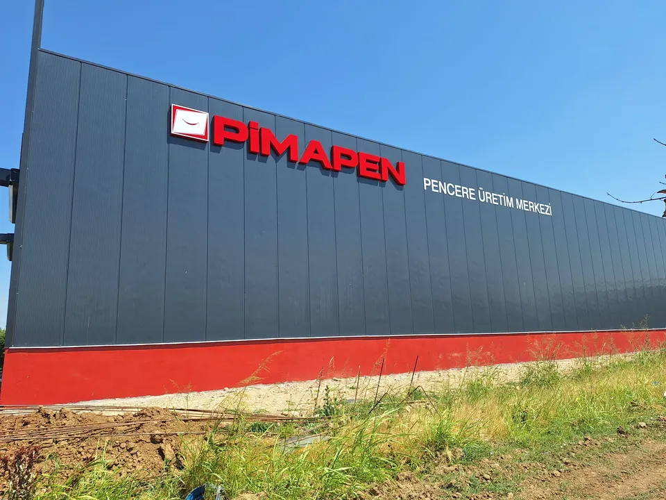 Pimapen logolu kırmızı-beyaz endüstriyel cephe tabelası, geniş gündüz görünümü.