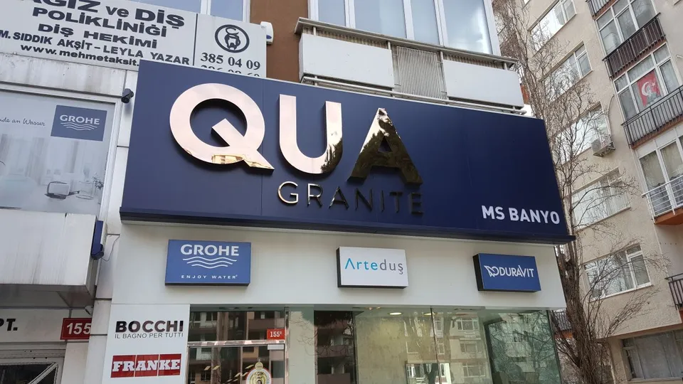 QUA Granite mağazasında antrasit zeminli büyük beyaz cephe harfleri.