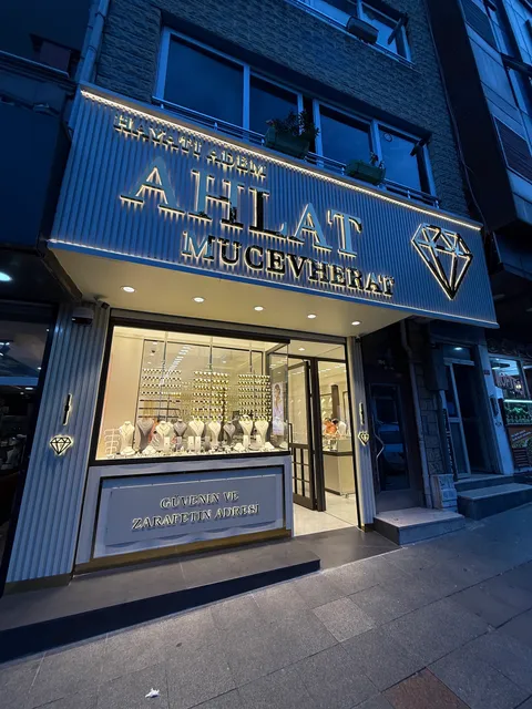 Hayati Adem Ahlat Mucevherat mağaza cephesinde dikey lamelli panoda arkadan ışıklı altın renkli harfler ve elmas logo, alacakaranlıkta karşıdan görünüm.