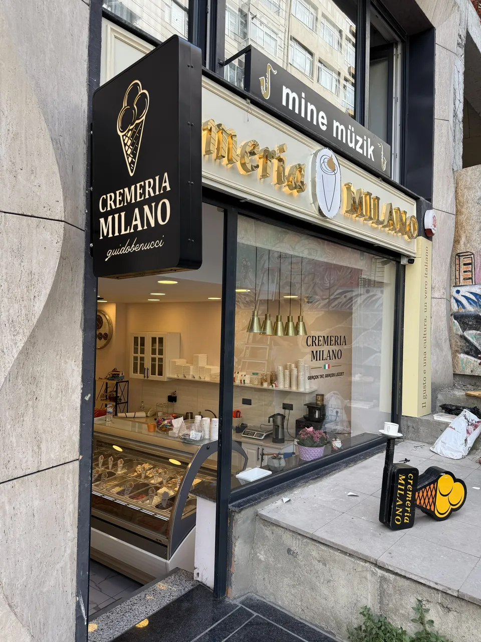 Cremeria Milano mağazasında siyah-altın dikey fener tabela ve cephe harfleri.