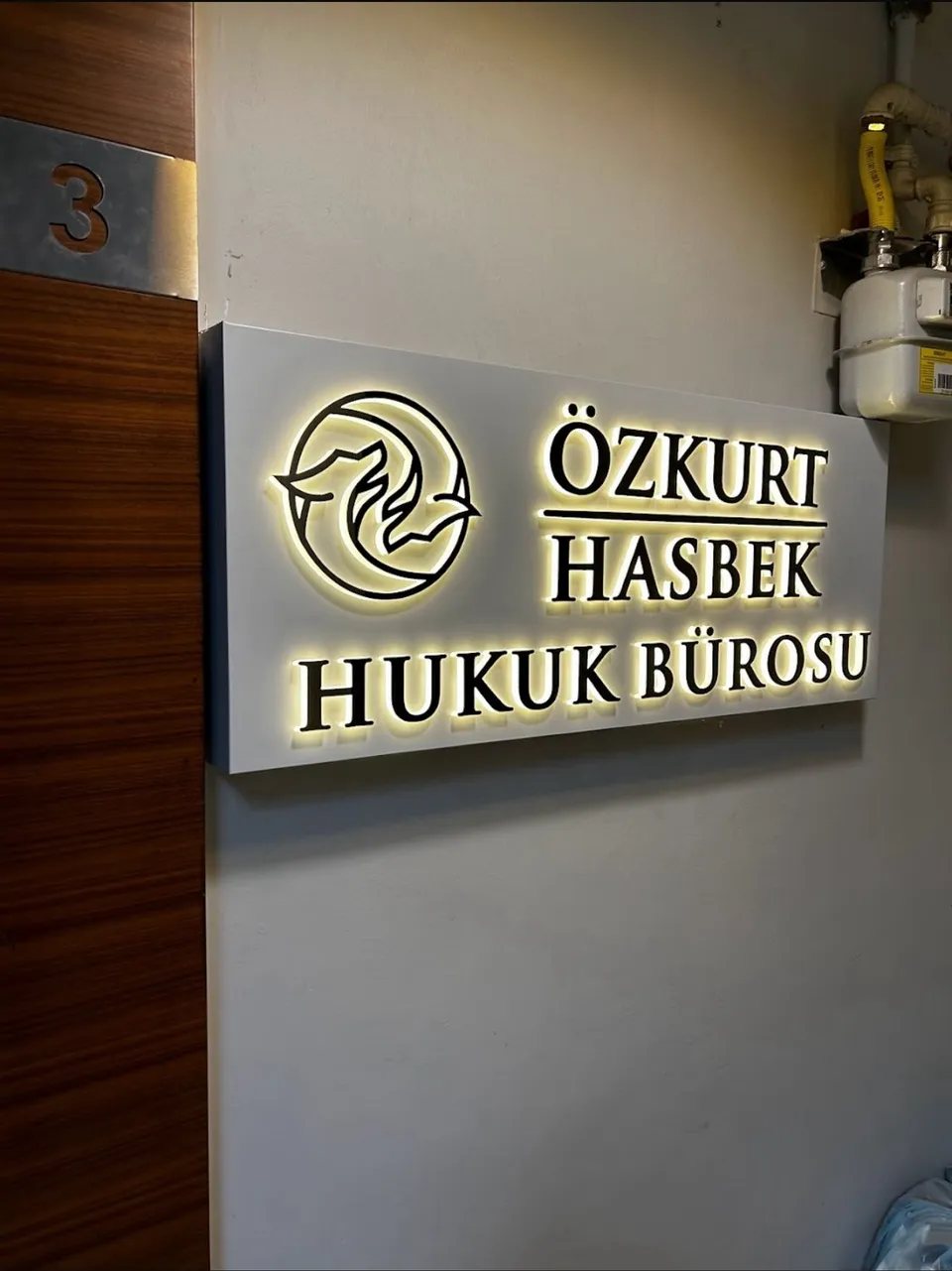 Özkurt Hasbek Hukuk Bürosu için duvara monte beyaz ışıklı logo ve isim tabelası.