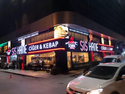Şiş Hane Ciğer & Kebap restoranının köşe cephesinde ışıklı beyaz harfler, kırmızı ışıklı şeritler ve ışıklı logo, gece görünümü.