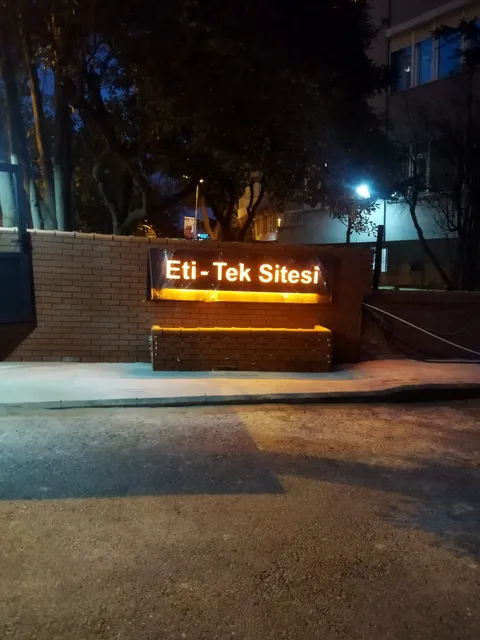 Eti-Tek Sitesi yazılı turuncu ışıklı harfli ve alttan aydınlatmalı tabela, tuğla duvarda gece görünümü.