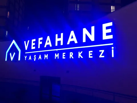 Vefahane Yaşam Merkezi yazılı beyaz ışıklı harfler ve açık mavi hatlı ev biçimli logo, duvara mavi ışık yansımalı gece görünümü.