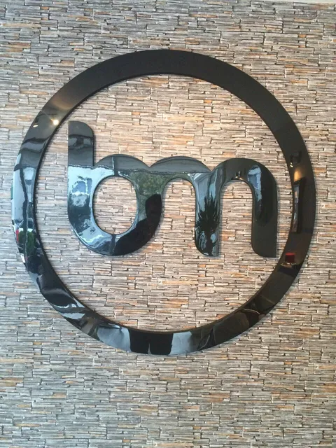 Taş kaplama duvarda parlak siyah pleksi bm logosu ve çember, dikey önden görünüm.