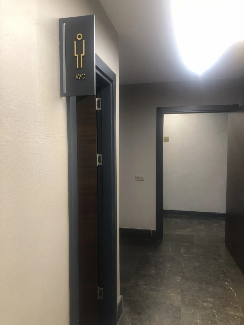 Ofis koridorunda siyah zeminli altın WC yönlendirme ve kapı isimliği.