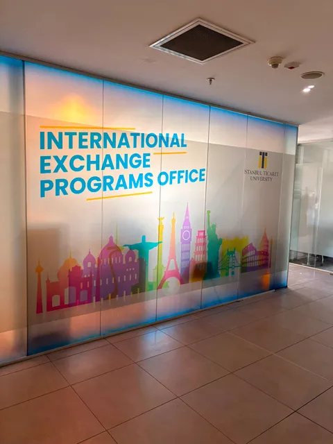 İstanbul Ticaret University logolu ve International Exchange Programs Office yazılı, dünya simgesi yapıların renkli silüetlerini taşıyan buzlu cam folyo uygulaması, koridordan görünüm.