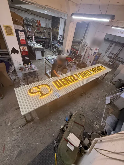 Deniz Parla Beauty için çizgili açık renkli panel üzerinde arkadan sarı ışıklı koyu harfler ve CD monogramı, üretim aşamasında yukarıdan geniş görünüm.