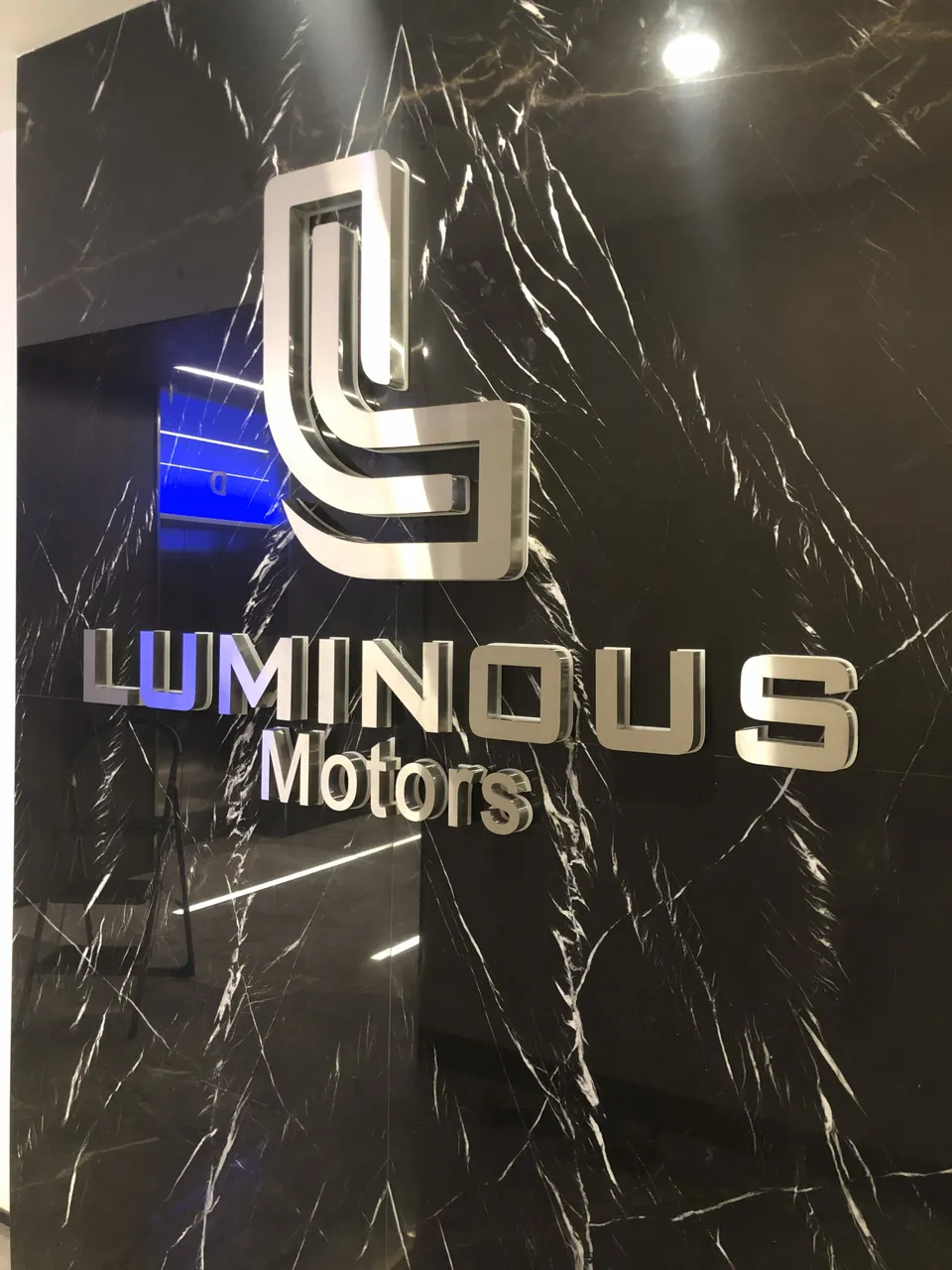 Luminous Motors için siyah mermer duvarda gümüş paslanmaz logo ve harfler.