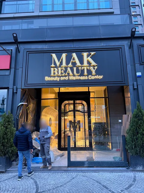 Mak Beauty girişinde siyah panel üzerinde ışıklı altın aynalı harfler ve Beauty and Wellness Center yazısı, alacakaranlıkta karşıdan görünüm.