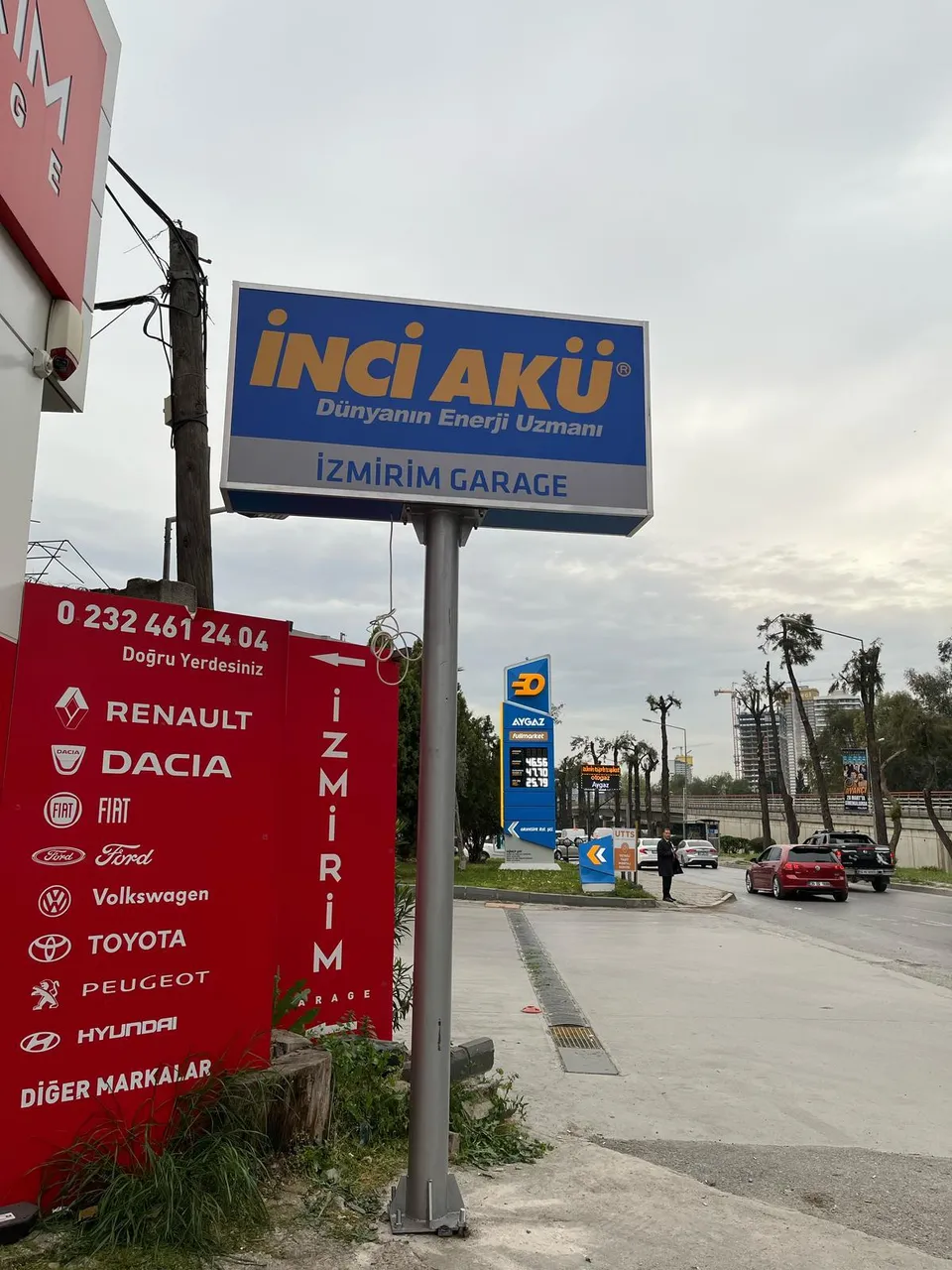 İnci Akü totemi ve kırmızı Renault Dacia servis yönlendirme panosu, yol kenarı görünümü.