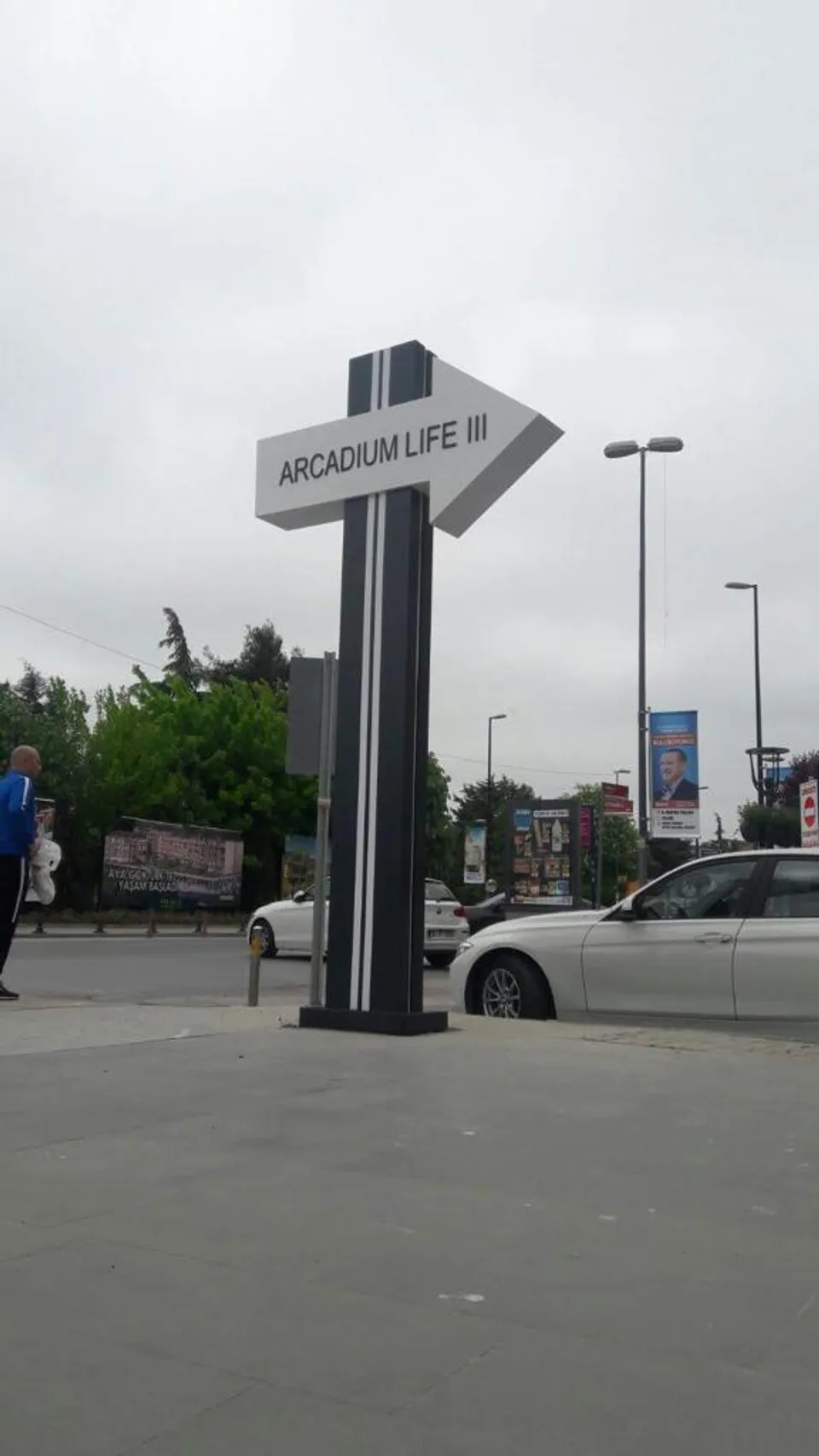 Otopark girişinde gri yönlendirme totemi, karşıdan gündüz görünümü.