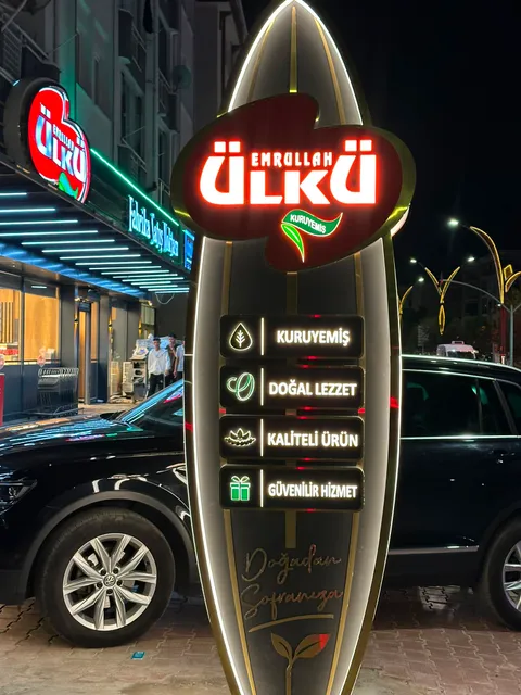 Emrullah Ülkü Kuruyemiş için ışıklı totem ve mağaza cephesindeki kırmızı logo, kaldırımdan yakın gece görünümü.